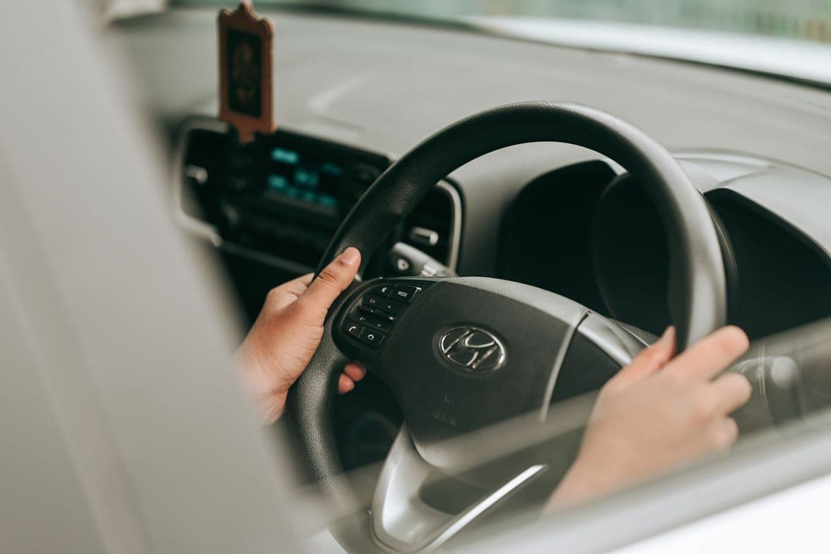 A driver's hands on a car steering wheel, seen through the open driver's window