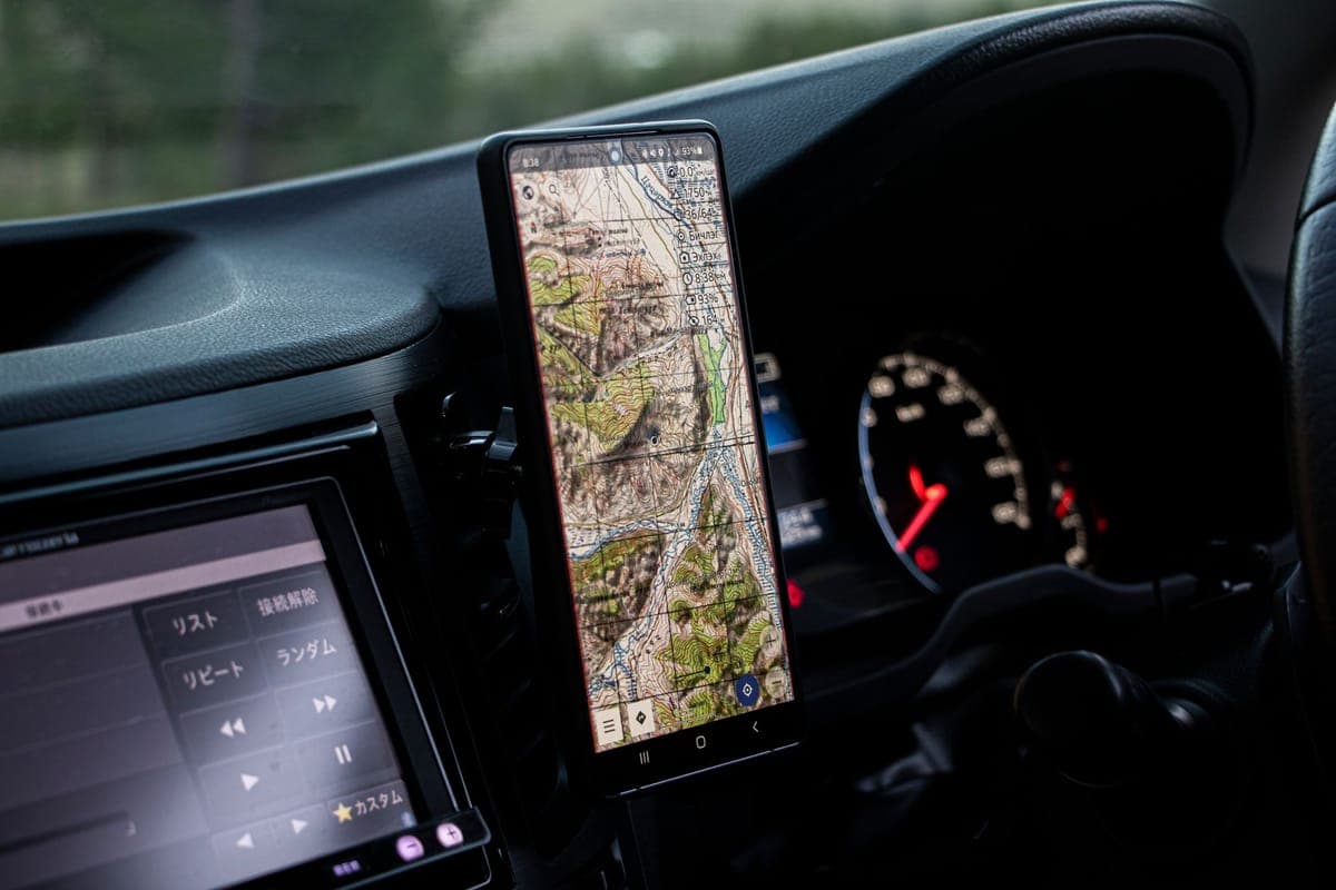 A phone held in a vent-clip car mount showing a map, beside the instrument cluster